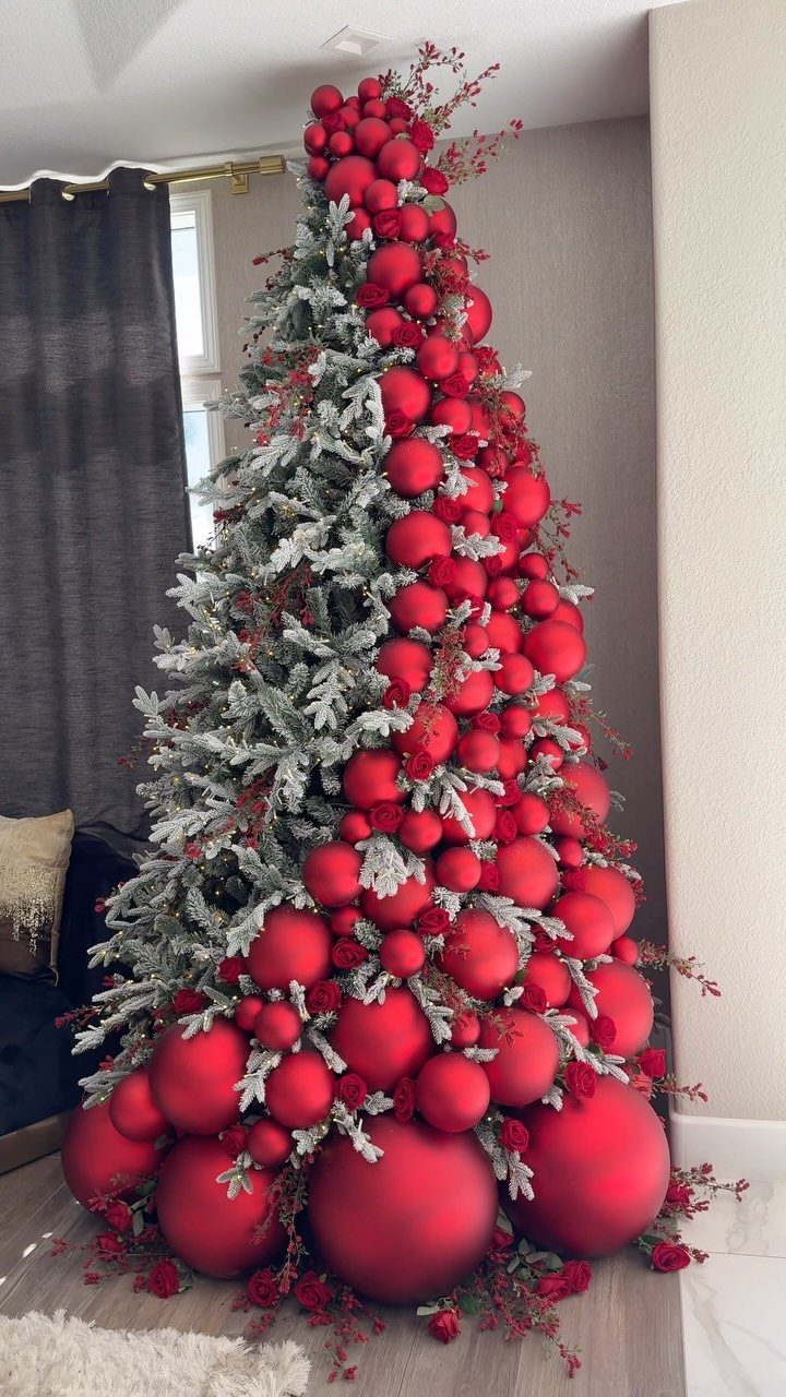 A flocked Christmas tree decorated with many large and small red ornaments.