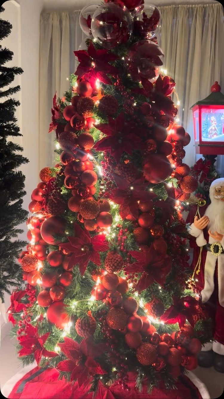 A Christmas tree densely decorated with red ornaments, red poinsettias, and glowing warm white lights.