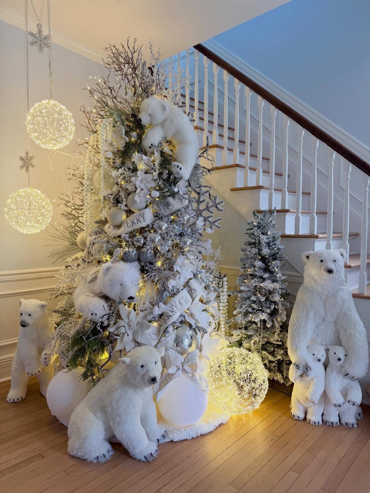 A white Christmas tree decorated with silver ornaments and large plush polar bear figures near a staircase.