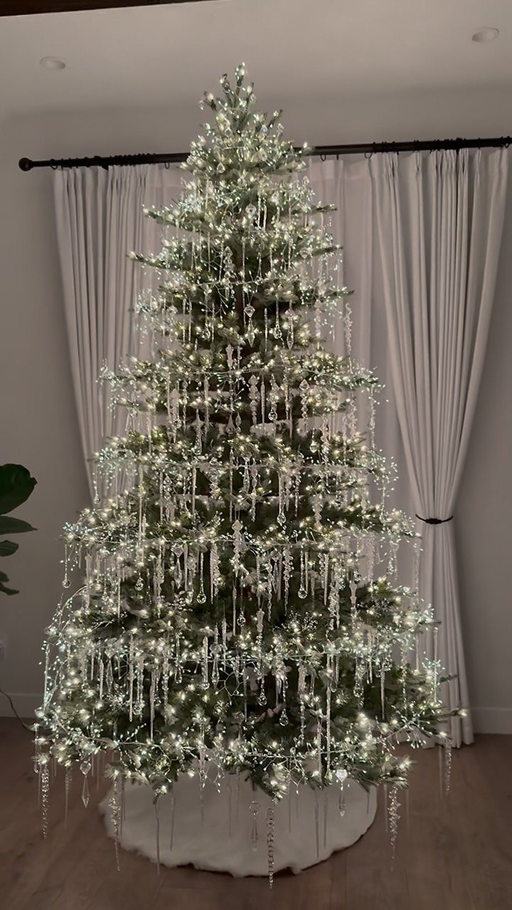 A lit Christmas tree decorated with long, shimmering silver icicle ornaments and white lights.