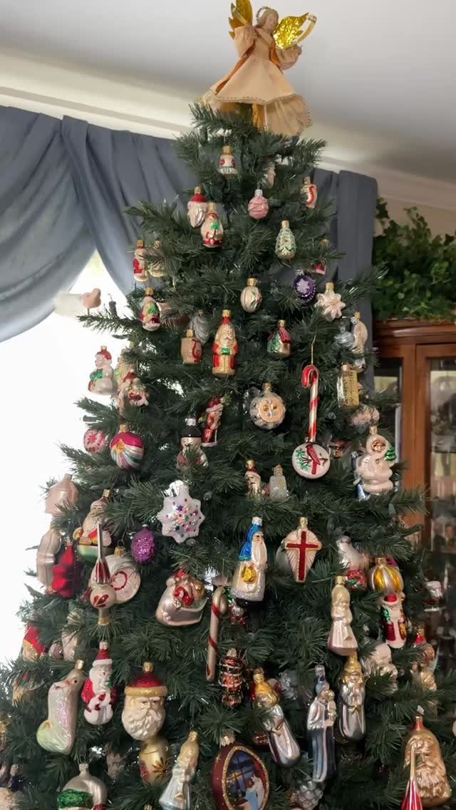 A Christmas tree adorned with many colorful vintage glass ornaments and an angel topper.
