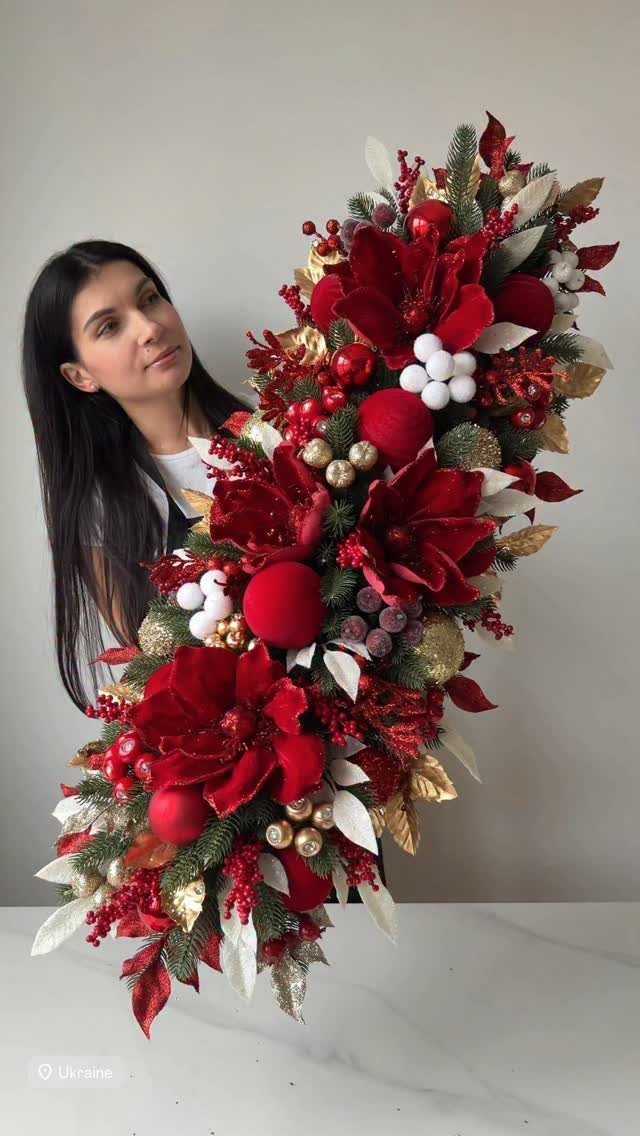 A woman holding a large decorative arrangement of red flowers, gold leaves, and festive berries.