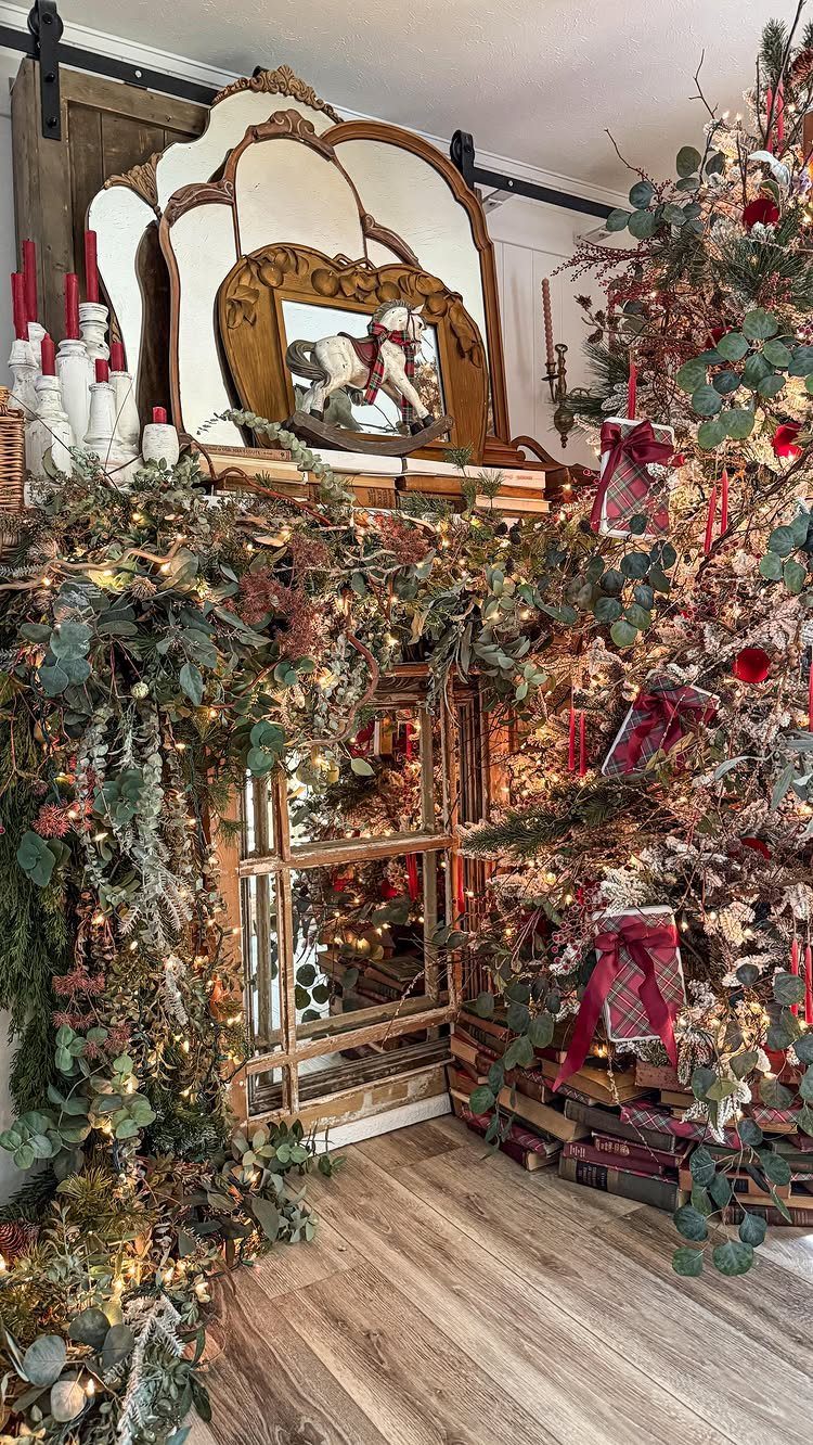 Christmas tree with red bows and a lit garland draped over a vintage wooden mirror.