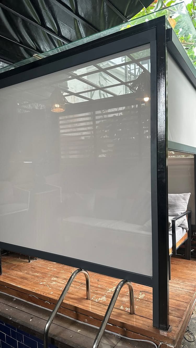 Black metal privacy structure with white screens on a wooden pool deck next to blue tiles.
