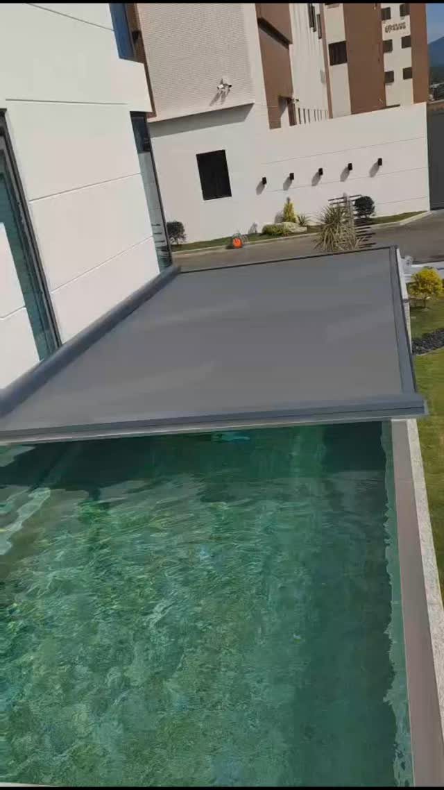 A grey retractable awning provides shade over the edge of a turquoise swimming pool.