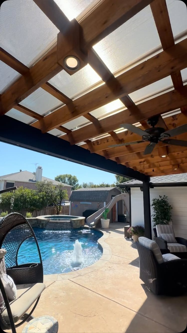Wooden pergola with translucent roofing overlooking a swimming pool and outdoor patio furniture.