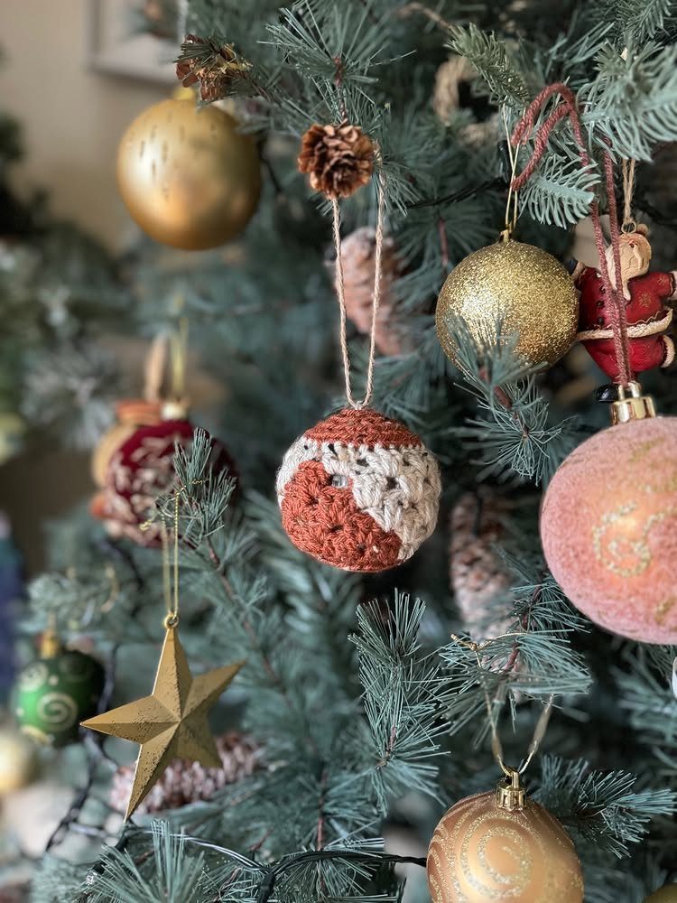Crochet Christmas Ornaments: 19 Free Patterns for 2026 2 A red and white crocheted Christmas bauble ornament hanging on a decorated pine tree.