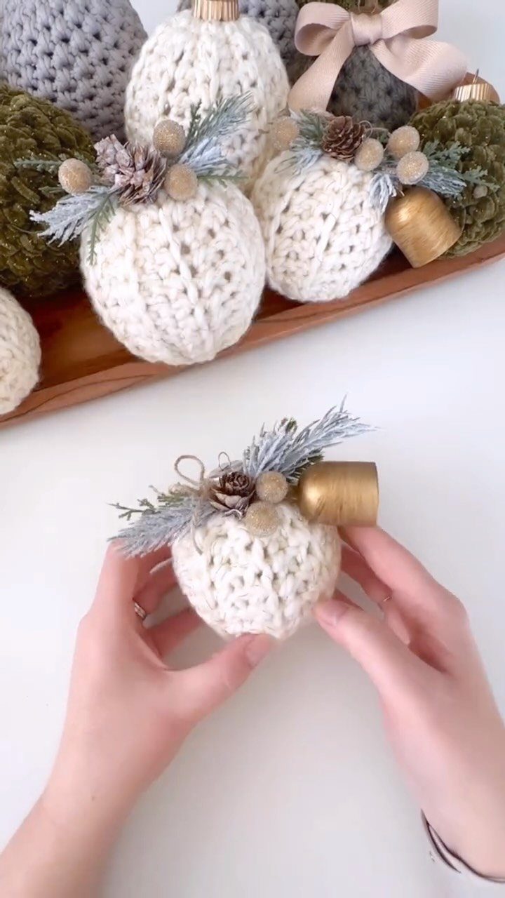 Crochet Christmas Ornaments: 19 Free Patterns for 2026 8 Hands holding a white crocheted round Christmas ball ornament with pinecone decorations.