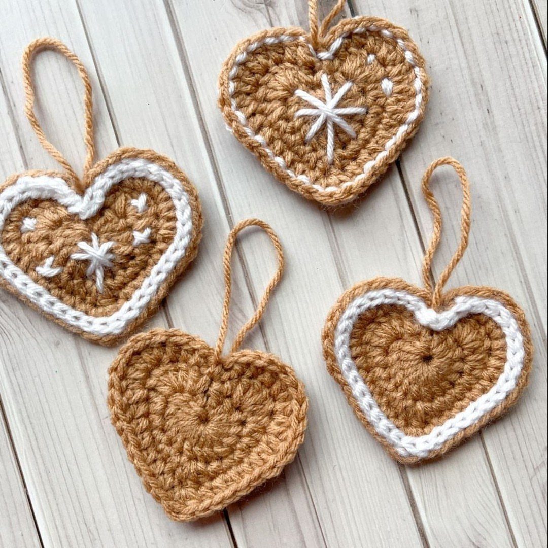 Crochet Christmas Ornaments: 19 Free Patterns for 2026 14 Four crochet heart-shaped gingerbread ornaments resting on a white wooden plank background.