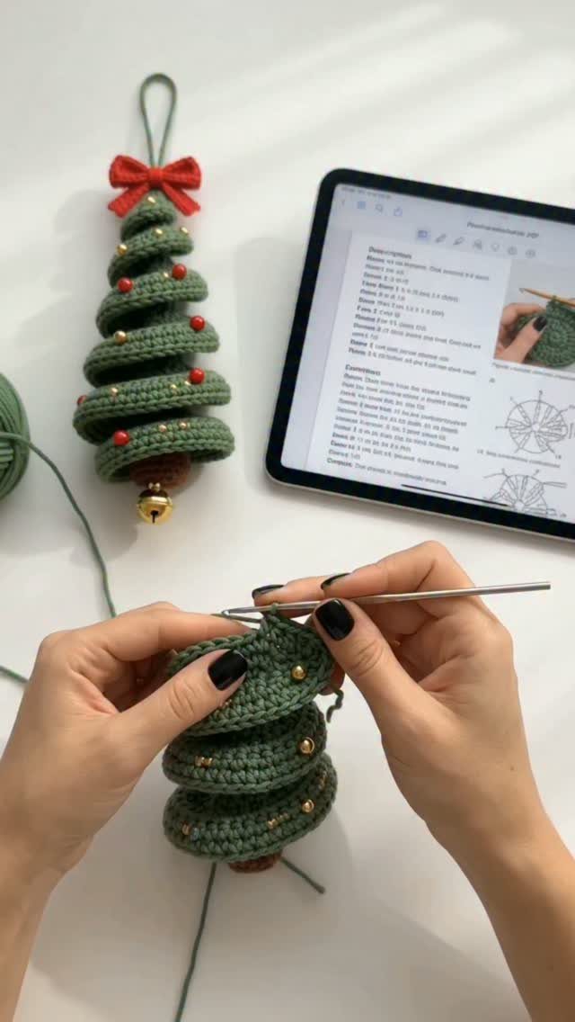 Crochet Christmas Ornaments: 19 Free Patterns for 2026 9 Hands crocheting a small green Christmas tree ornament with gold beads on a white surface.
