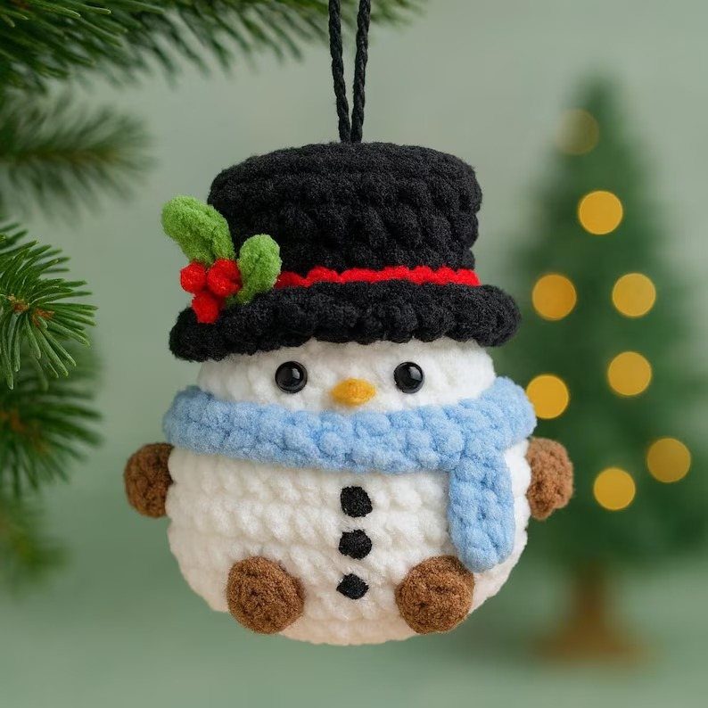 Crochet Christmas Ornaments: 19 Free Patterns for 2026 5 Crocheted snowman ornament with a black hat and blue scarf hanging from a green pine branch.