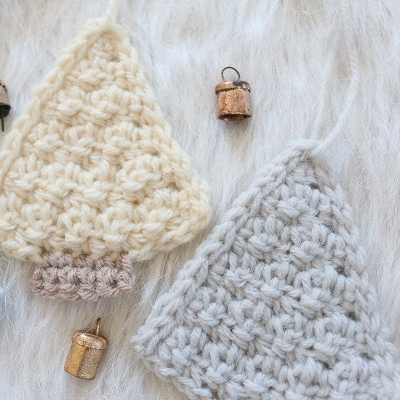 Two flat crocheted Christmas tree ornaments in cream and grey on white faux fur.