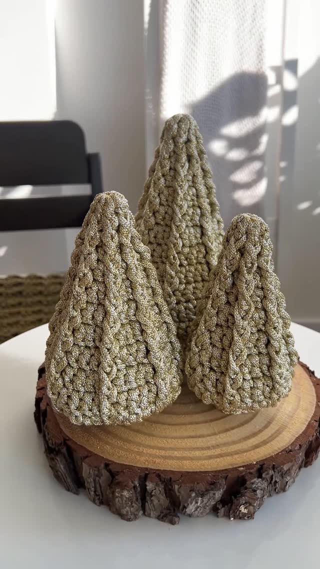 Three gold glittery crocheted Christmas trees of different sizes sitting on a wooden tree slice.
