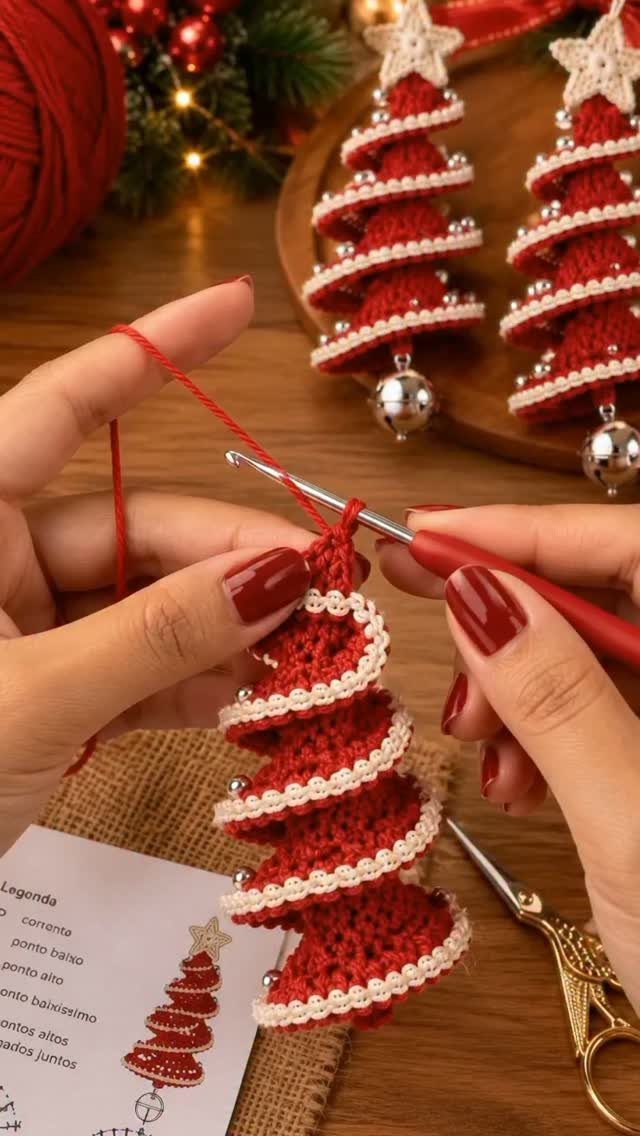 Hands crocheting a small red and white spiral-patterned Christmas tree ornament with a red hook.