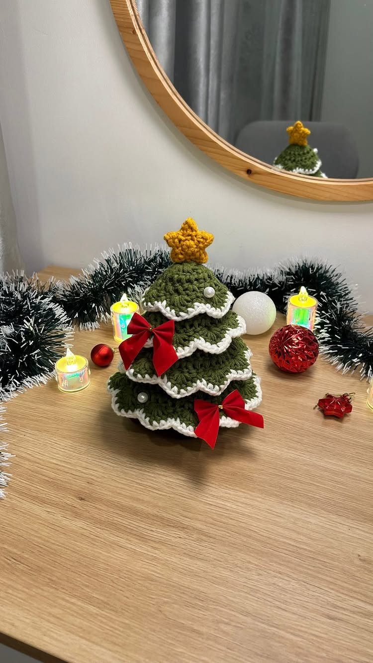 A small green crocheted Christmas tree with red bows and a yellow star on a wooden table.