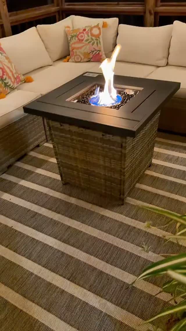 A striped outdoor rug under a wicker fire pit and white sectional sofa.