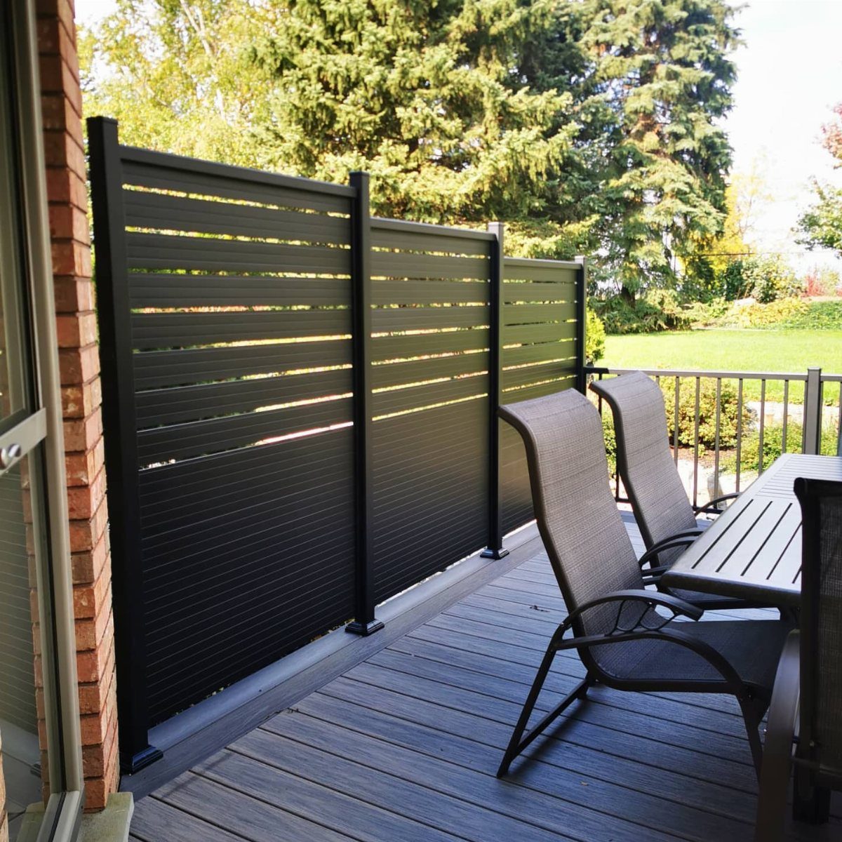 Black horizontal slat privacy screen installed on a wooden deck overlooking a green yard.