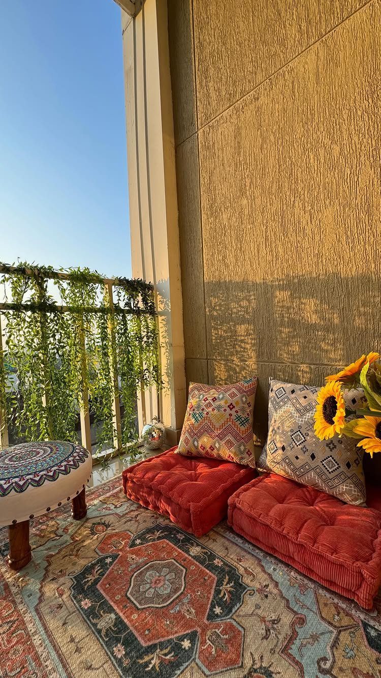 Red floor cushions and patterned pillows arranged on a rug on a decorated balcony.