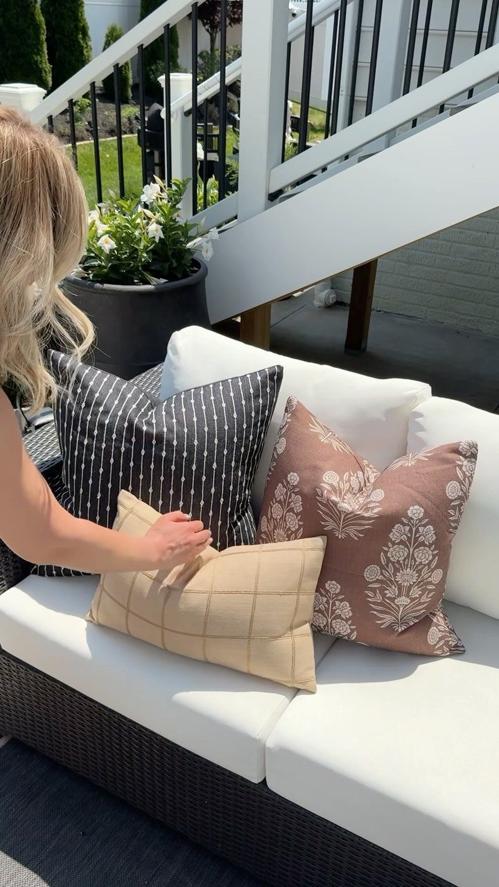 Hands arranging patterned throw pillows on a white outdoor sofa on a deck.