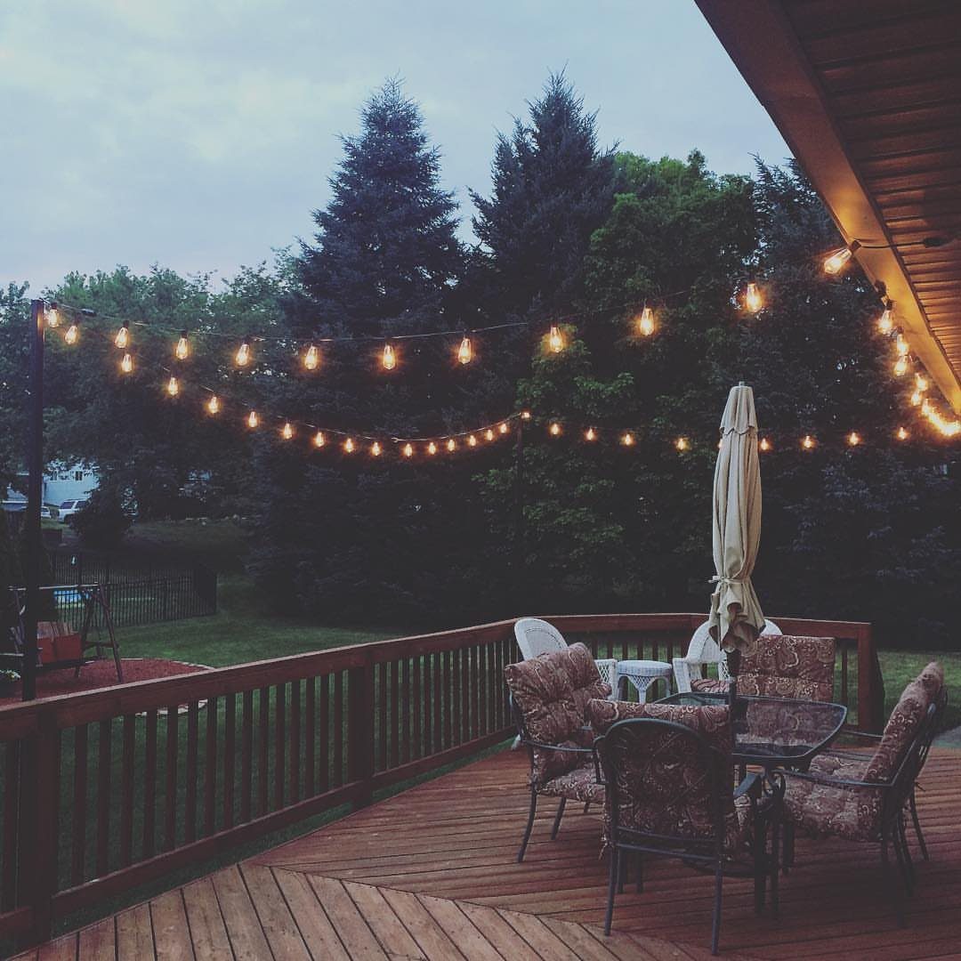 Glowing string lights draped across a wooden deck with patio furniture and trees in the background.
