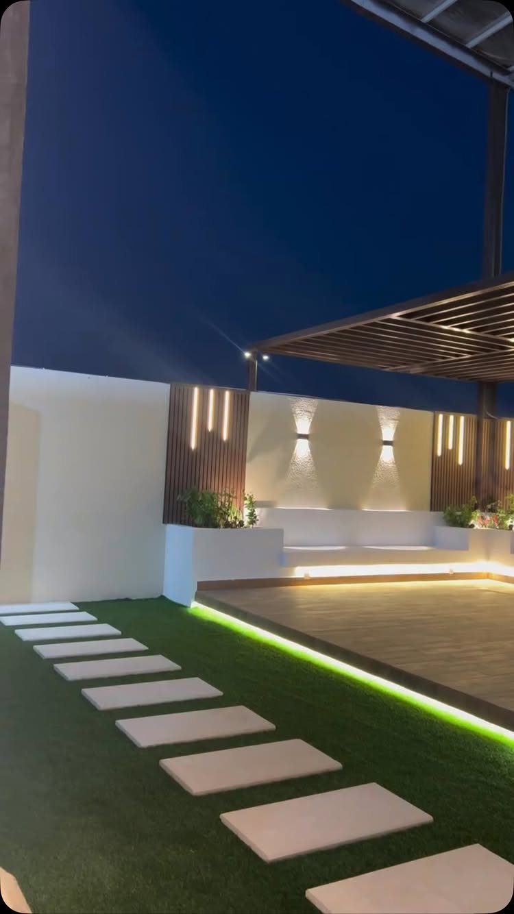 Modern outdoor deck with wooden platform, artificial grass, stepping stones, and glowing LED strip lighting.