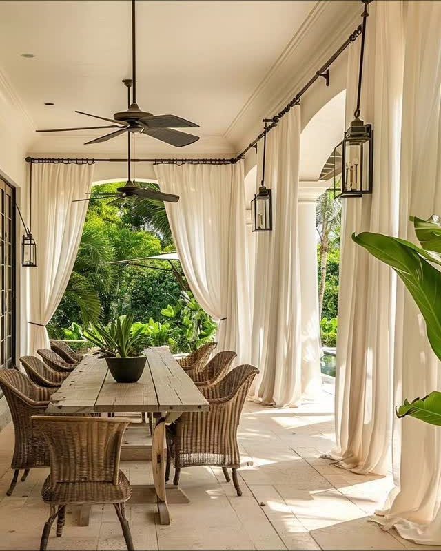 White flowing curtains framing a wooden dining table on a covered tropical patio.