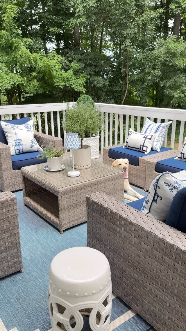 Wicker patio furniture with blue cushions and white patterned throw pillows on a wooden deck.