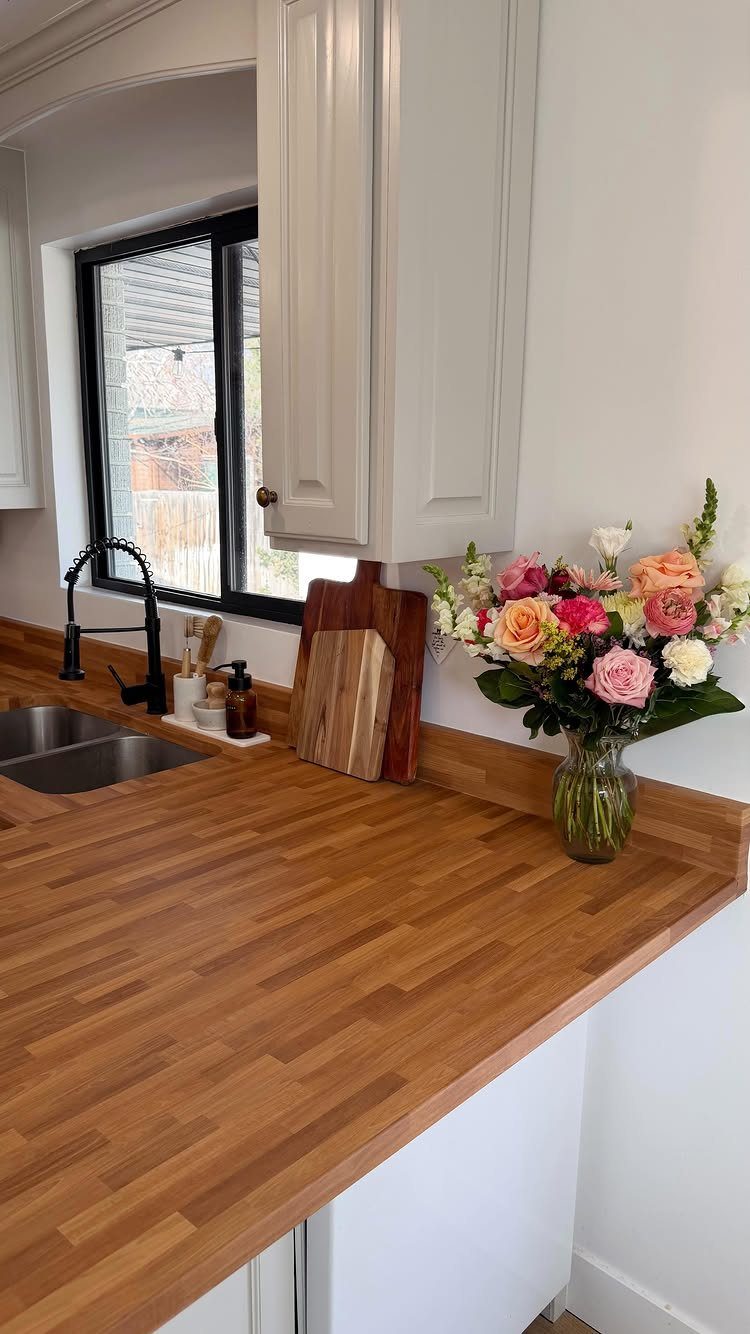 6 DIY Kitchen Countertops That Cost Less Than You Expect 2 Butcher block wooden countertops in a kitchen with a sink and flowers.