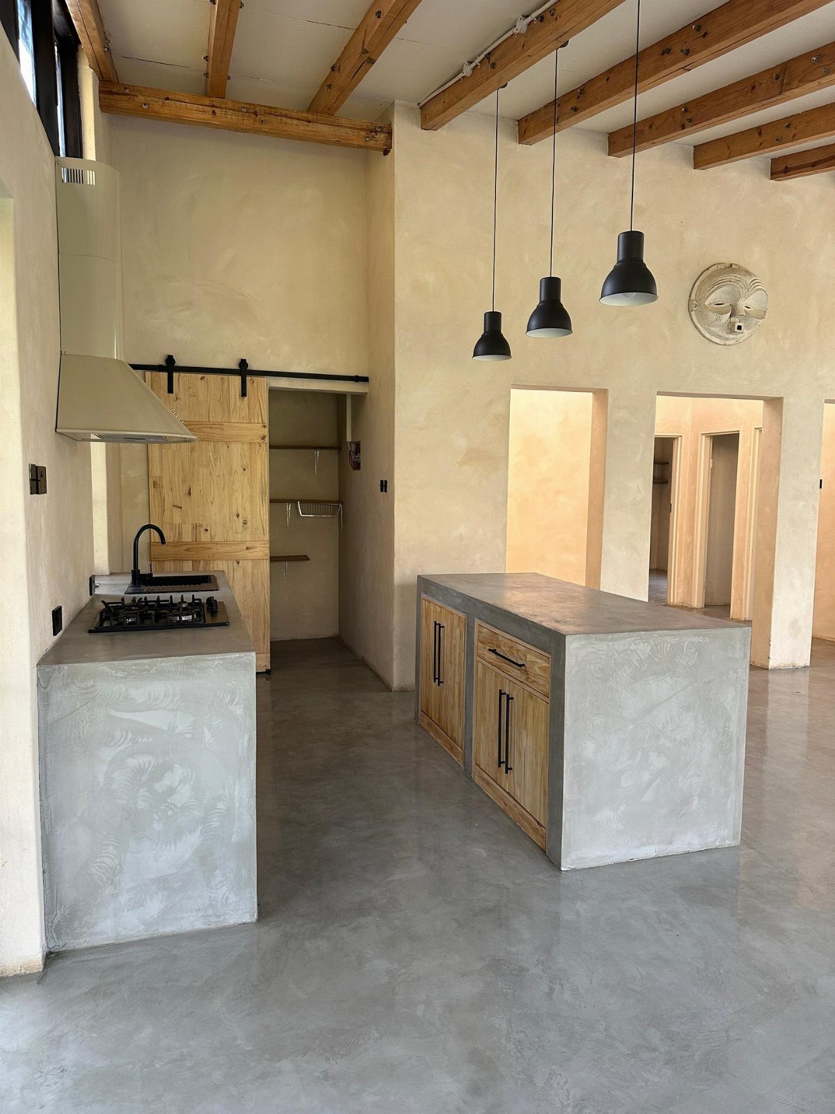 6 DIY Kitchen Countertops That Cost Less Than You Expect 1 Concrete kitchen island with wooden cabinets under exposed wooden ceiling beams in a modern room.