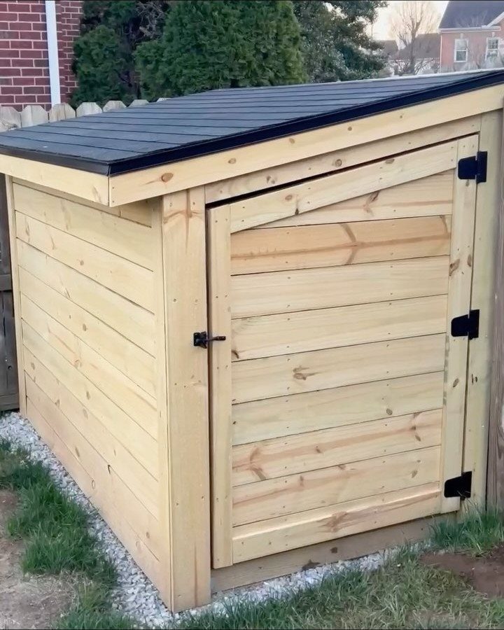 DIY Modern Shed: 19 Plans for Every Yard and Budget 18 A small wooden storage shed with a black slanted roof sitting on gravel next to grass.