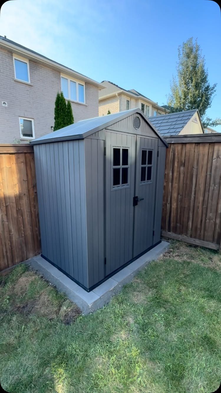 DIY Modern Shed: 19 Plans for Every Yard and Budget 6 A dark grey modern storage shed sits on a concrete slab foundation in a backyard.