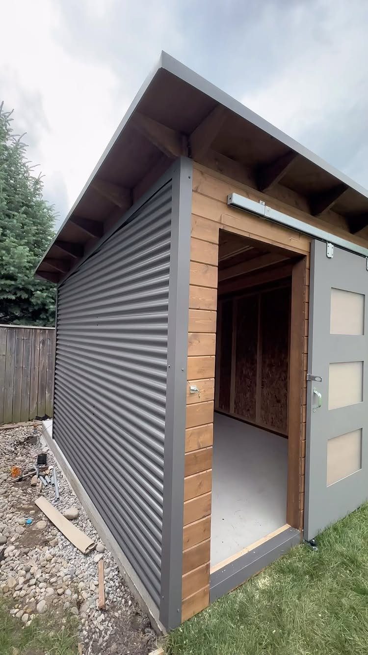 DIY Modern Shed: 19 Plans for Every Yard and Budget 13 A modern garden shed with grey corrugated metal walls and natural wood trim standing on grass.