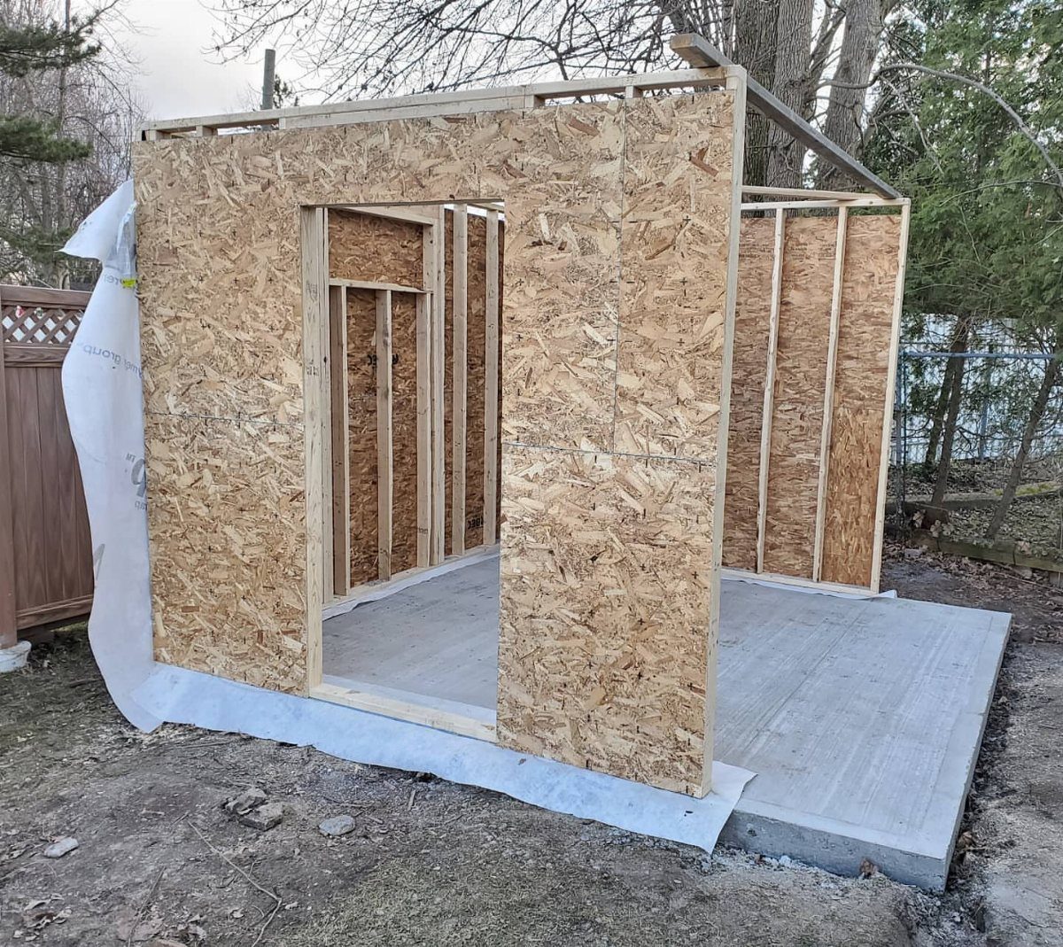 DIY Modern Shed: 19 Plans for Every Yard and Budget 1 Wooden shed walls under construction with exposed framing and OSB sheathing on a concrete slab.