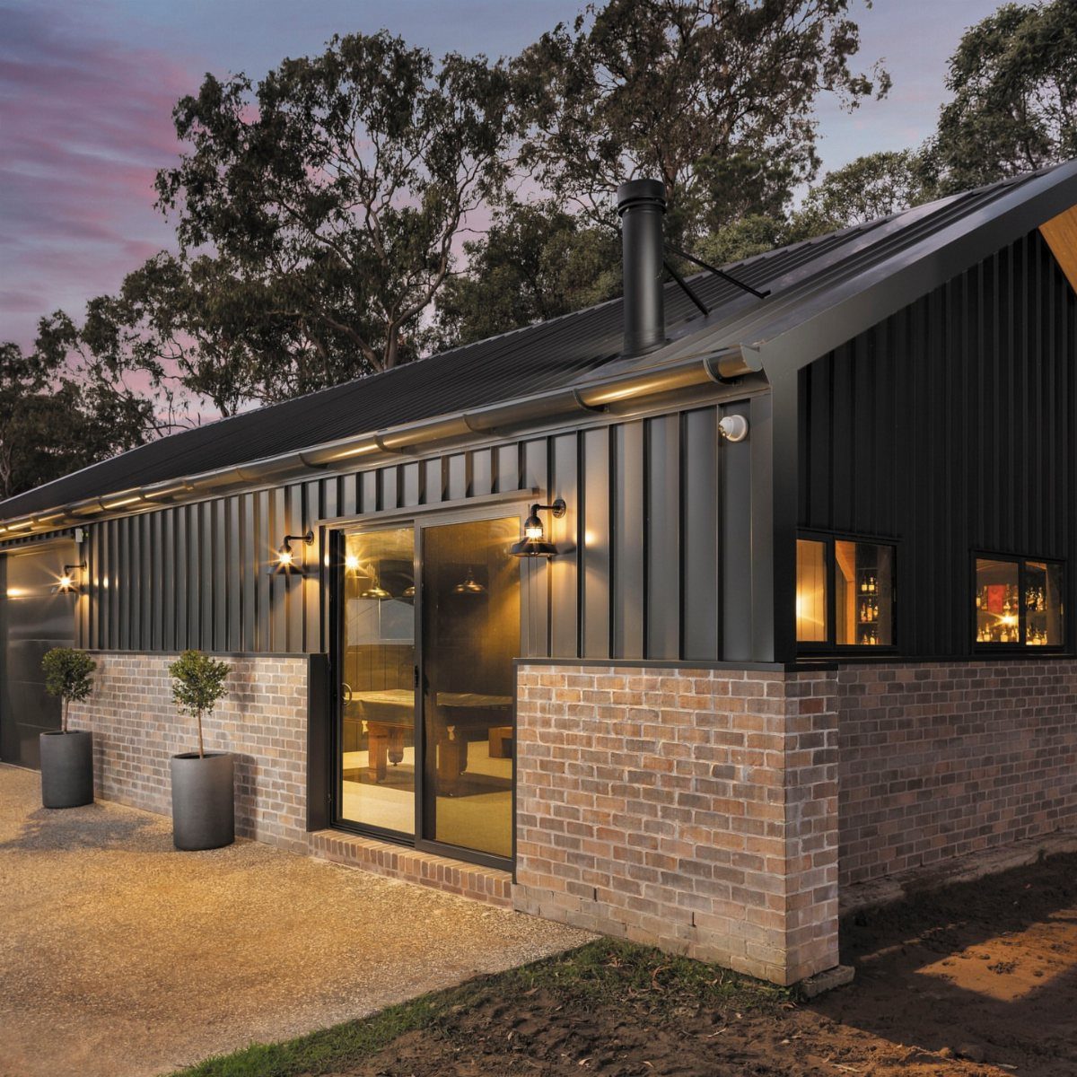 DIY Modern Shed: 19 Plans for Every Yard and Budget 7 Modern black shed featuring vertical metal siding and a brick foundation under a twilight sky.