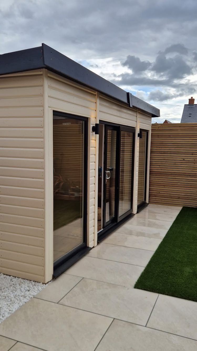 DIY Modern Shed: 19 Plans for Every Yard and Budget 5 A modern cream wooden garden shed with large black glass doors on a stone patio.