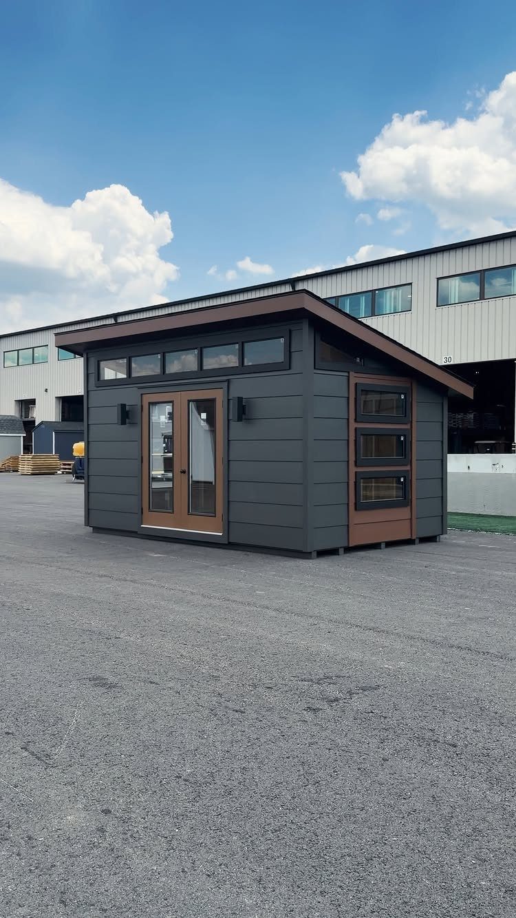 DIY Modern Shed: 19 Plans for Every Yard and Budget 10 A modern dark grey garden shed with wood-trimmed glass doors and windows on gravel.