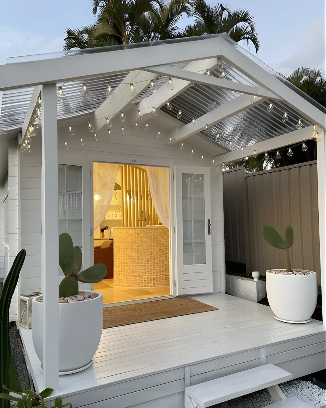 DIY Modern Shed: 19 Plans for Every Yard and Budget 19 A white modern shed with a translucent roof, string lights, and potted cacti on a wooden deck.