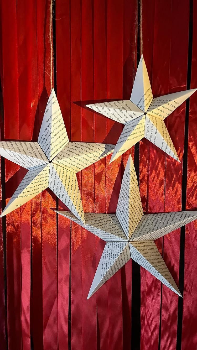 Three star ornaments made from book pages hanging against a red textured fabric background.