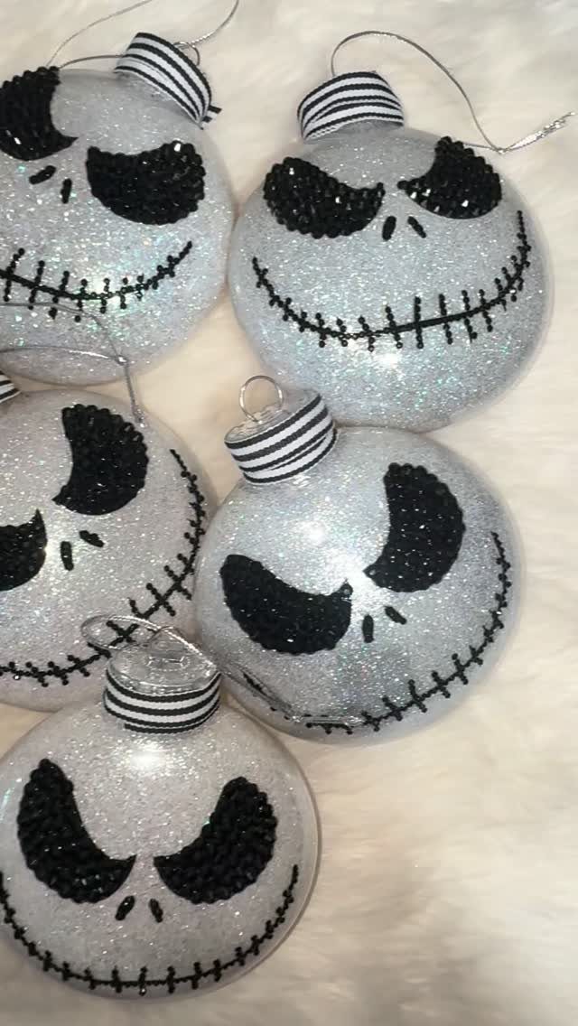 Five Jack Skellington themed glittery white Christmas ornaments resting on white faux fur.