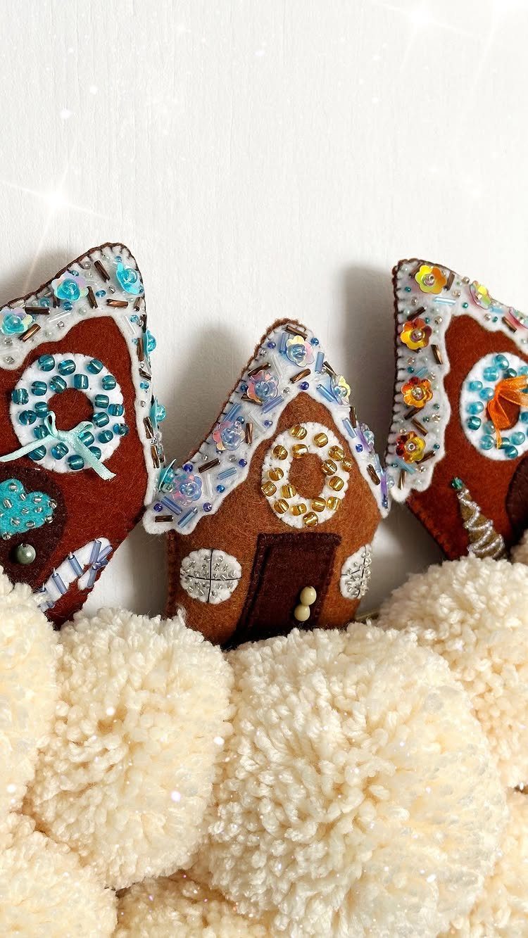 Three gingerbread house shaped felt ornaments decorated with colorful sequins and beads on white pom-poms.