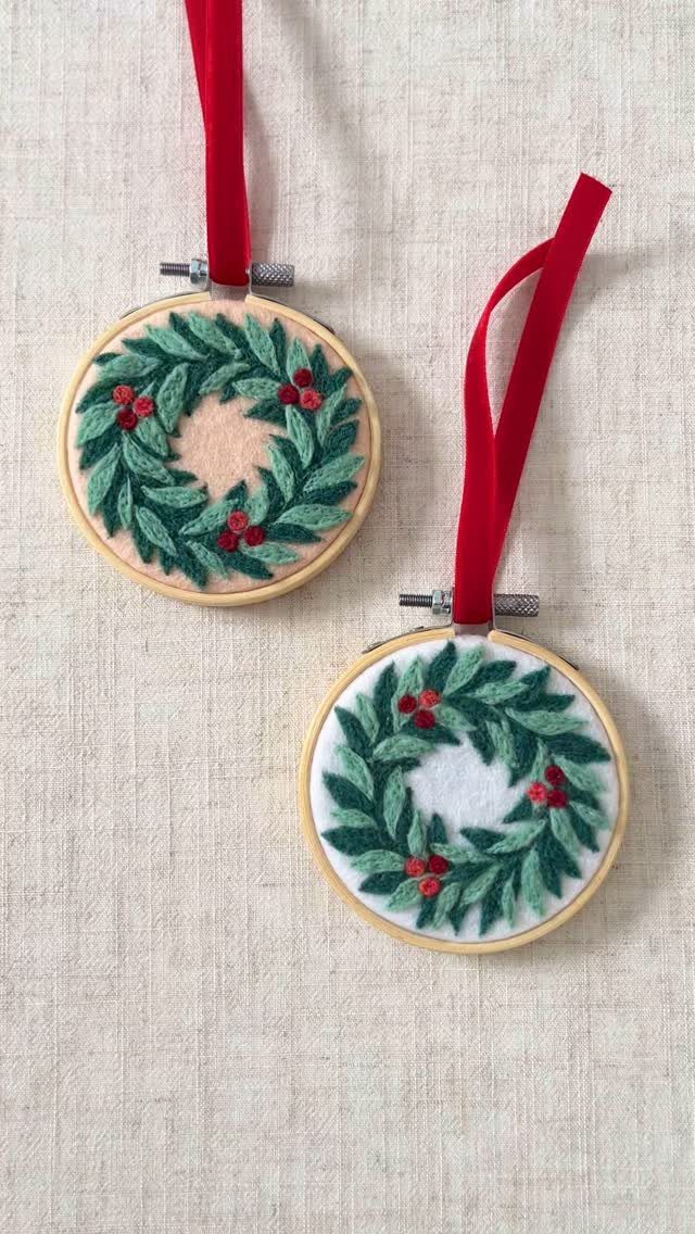 Two small felt wreath ornaments in wooden embroidery hoops hanging by red ribbons.