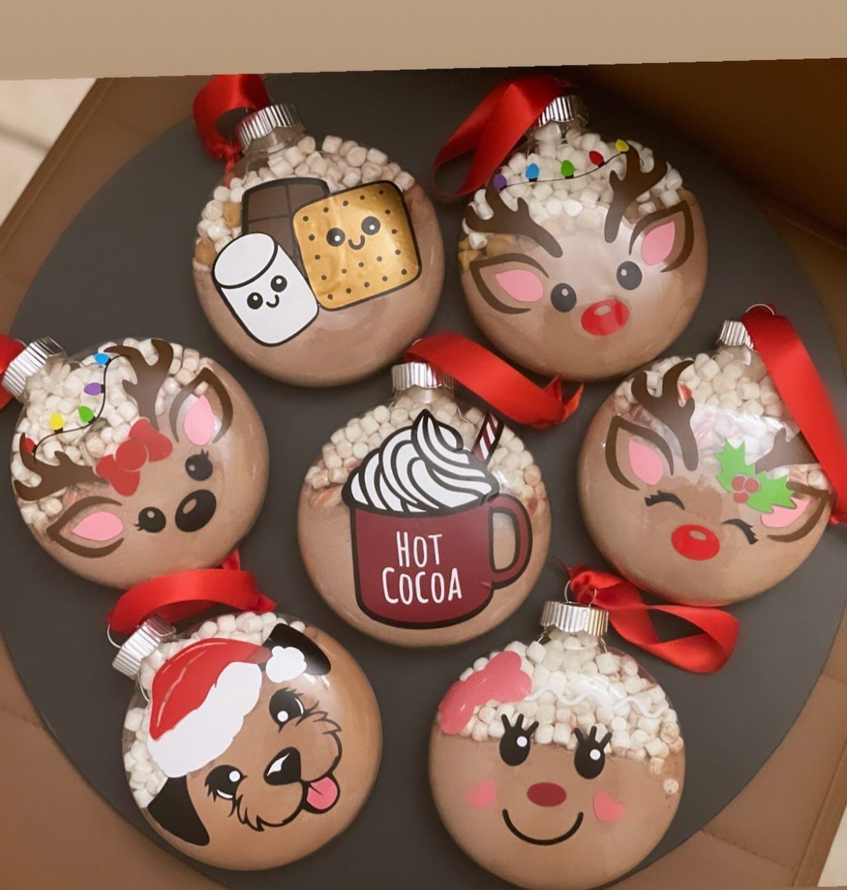 Seven clear ornaments filled with cocoa powder and marshmallows, featuring various cute cartoon character designs.