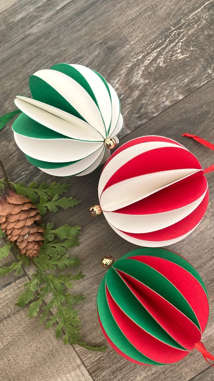 Three striped paper sphere ornaments in green, red, and white on a wooden surface.