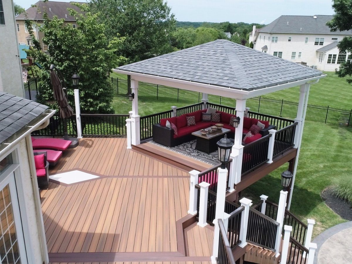 11 Elevated Deck Ideas: Multi-Level Looks, Storage & Rooftop Builds 11 A large wooden multi-level deck with a covered gazebo and red outdoor furniture overlooking a green yard.