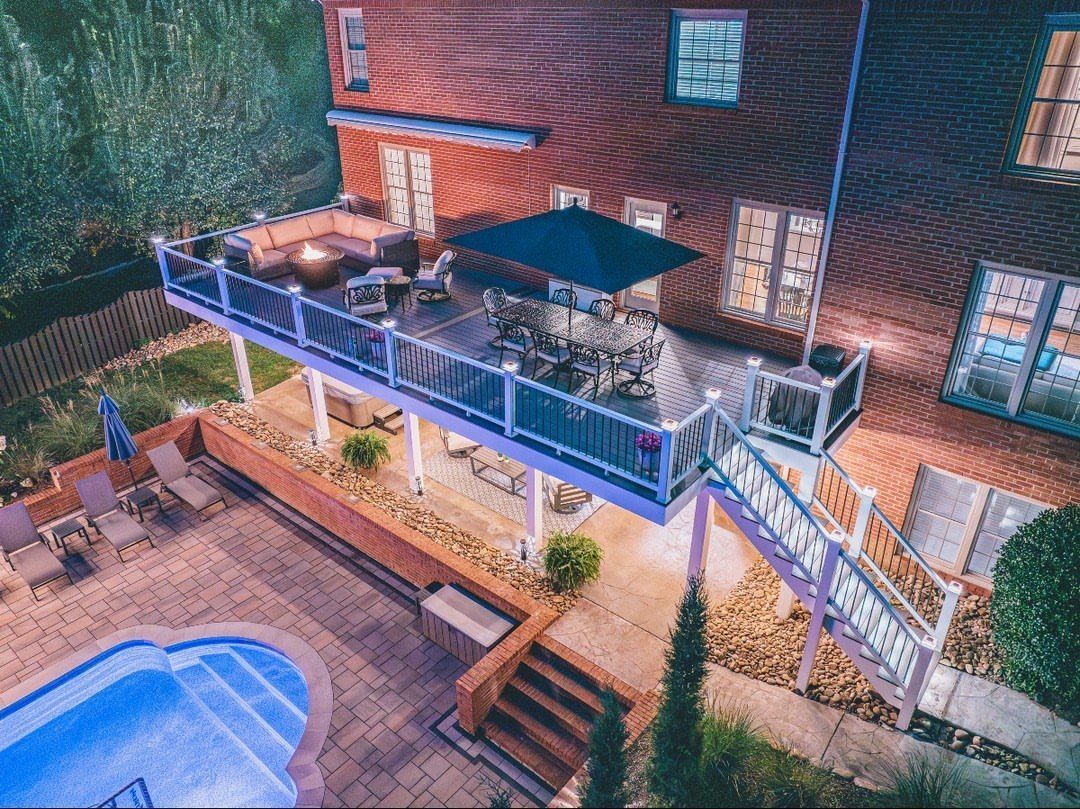 11 Elevated Deck Ideas: Multi-Level Looks, Storage & Rooftop Builds 8 An elevated wooden deck with white railings, outdoor furniture, and a dining set attached to a brick house.