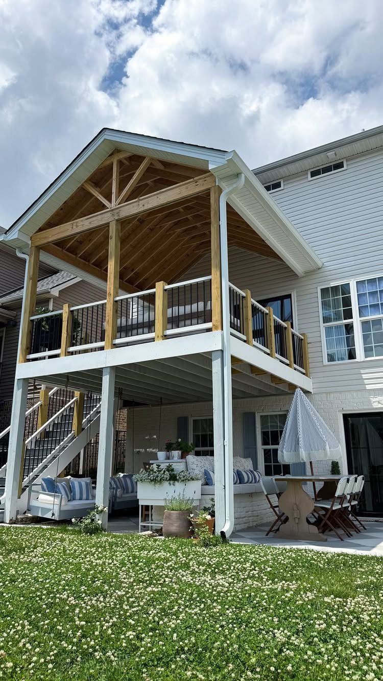 11 Elevated Deck Ideas: Multi-Level Looks, Storage & Rooftop Builds 9 A large two-story wooden deck with a gabled roof and a covered patio area overlooking a green lawn.