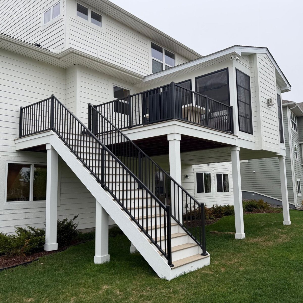 11 Elevated Deck Ideas: Multi-Level Looks, Storage & Rooftop Builds 3 Elevated white wooden deck with black railings and a screened-in enclosure attached to a house.