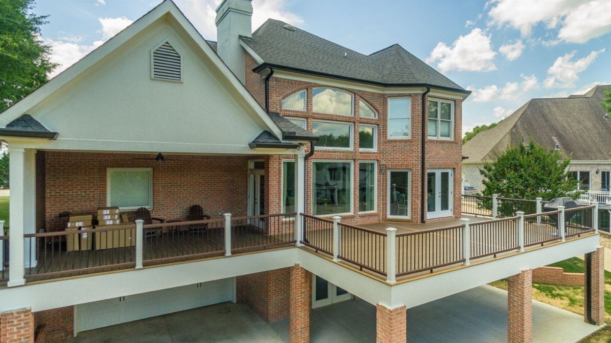 11 Elevated Deck Ideas: Multi-Level Looks, Storage & Rooftop Builds 10 Large elevated wooden deck with white railings attached to a two-story brick house.