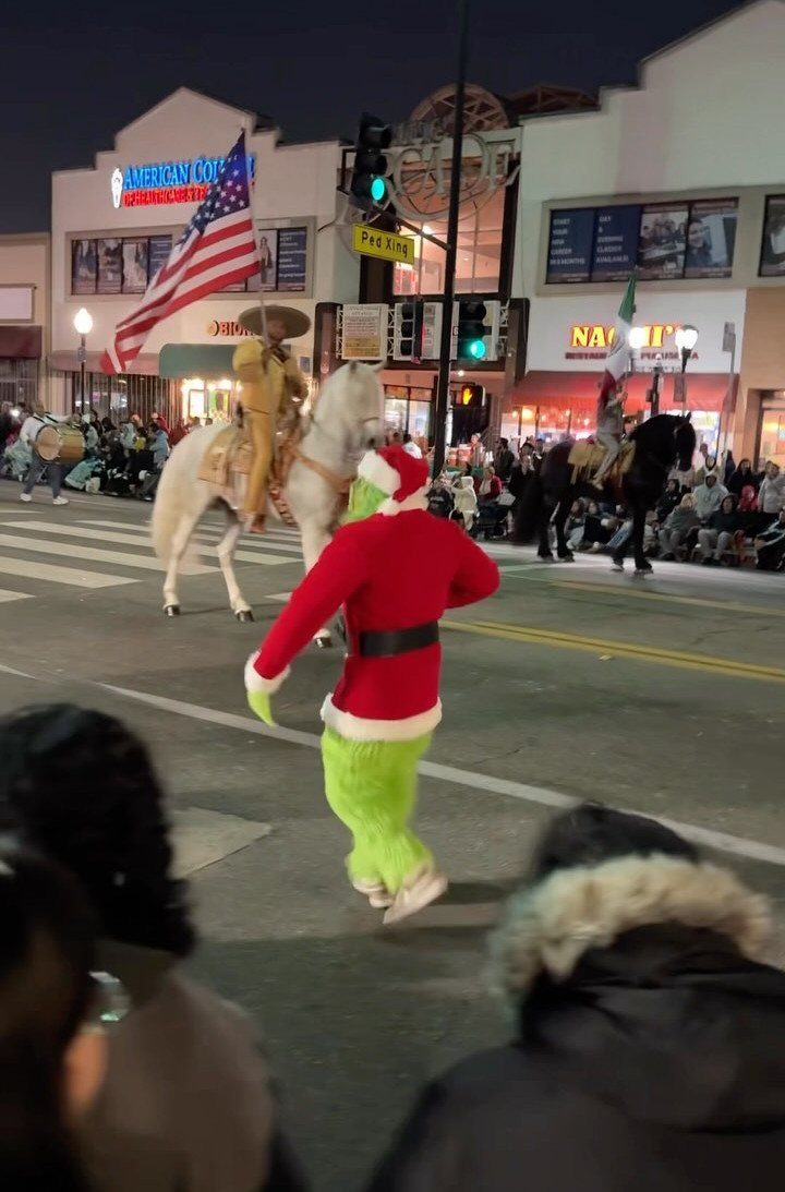 Fun Christmas Activities for Families: 18 Ideas With Photos 4 An elf in a red costume dances on a street during a nighttime holiday parade.