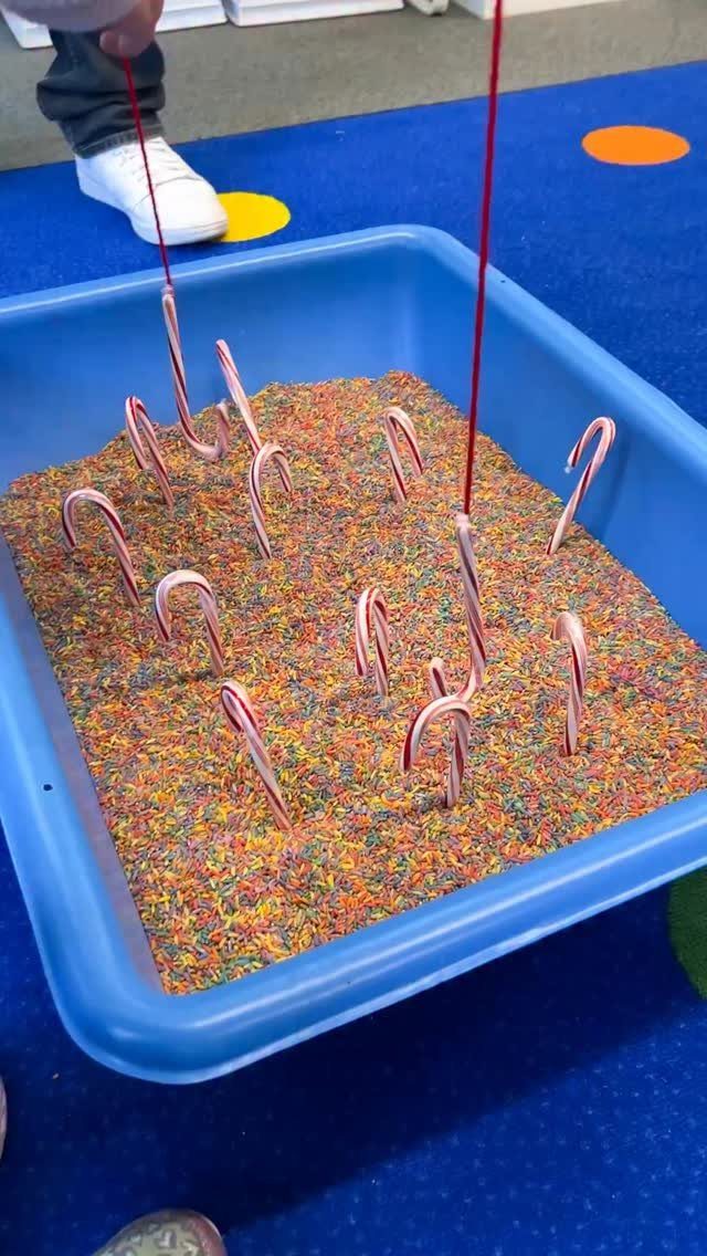 Fun Christmas Activities for Families: 18 Ideas With Photos 18 Candy canes stuck in colorful sensory grains inside a blue plastic bin being played with.